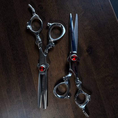 Pair of silver scissors with red gemstones on a dark wooden surface

