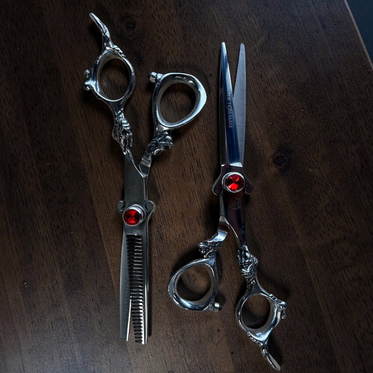 Pair of silver scissors with red gemstones on a dark wooden surface

